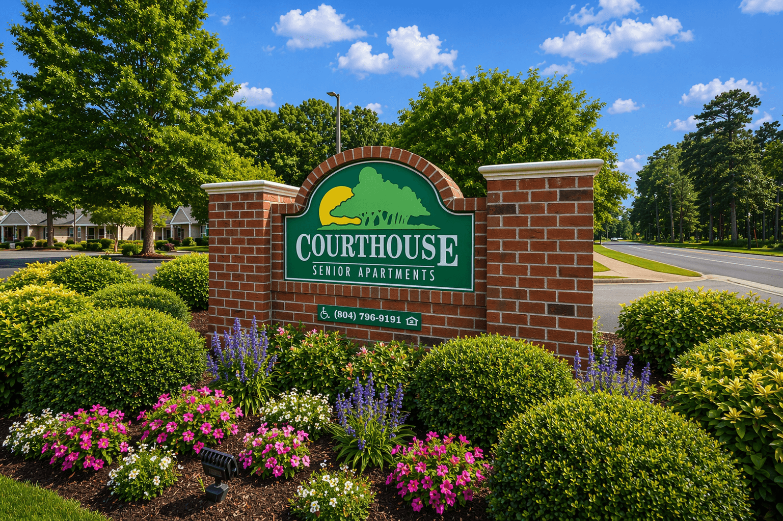 A sign for Courthouse Senior Apartments is surrounded by flowers and greenery.